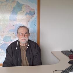Homem Branco, cabelo curto, jaqueta preta em frente ao computador.