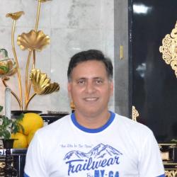 Homem Branco, cabelo preto curto, camisa branca e azul em ambiente social.