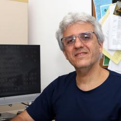 homem branco, com óculos de grau, camiseta preta junto no escritório.