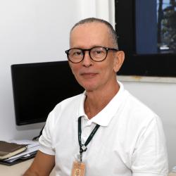 homem branco de camiseta branca e óculos de grau em escritório.