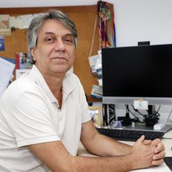 homem branco com camiseta branca, cabelos curtos em seu posto de trabalho.