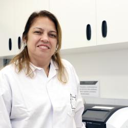 Mulher branca, cabelos claros, jaleco branco em ambiente de laboratório.