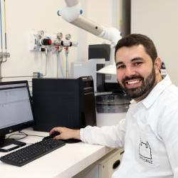 homem branco, cabelo preto curto, jaleco branco em ambiente de laboratório.
