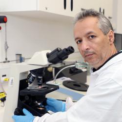 Homem branco, cabelo curto, jaleco branco em ambiente de laboratório.