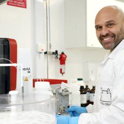 homem branco, com barba, jaleco branco em ambiente de laboratório.