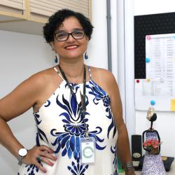 Mulher de cabelo preto ondulado e curto, vestido branco com azul, em ambiente de escritório.