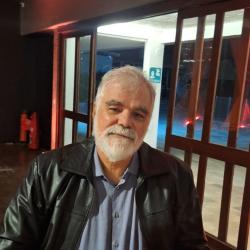 Homem branco de cabelo curto e barba, jaqueta preta e camisa azul.