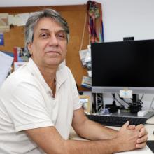 homem branco com camiseta branca, cabelos curtos em seu posto de trabalho.