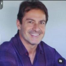 homem branco, cabelo escuro, camisa azul, sorrindo.