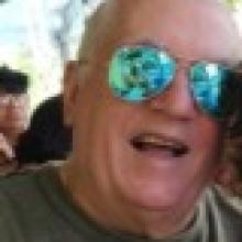 homem branco, de óculos de sol, cabelo curto branco e camisa verde.